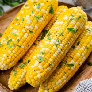 Roasted corn, topped with chopped parsley, on a wooden plate.